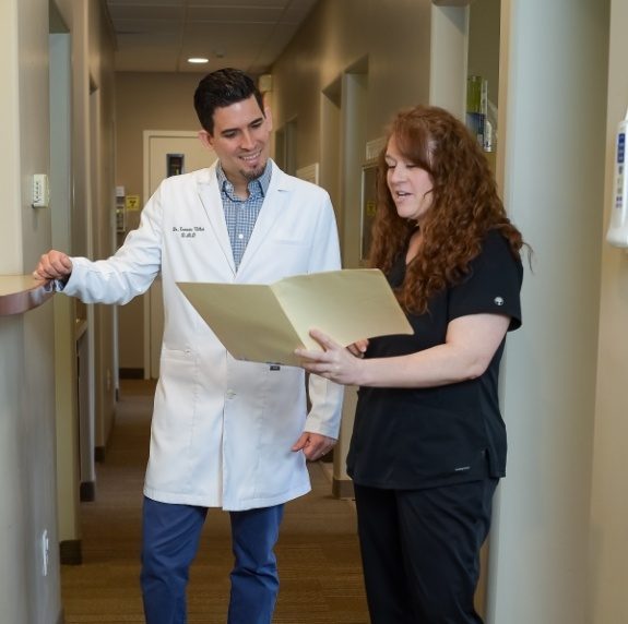 Dental team member showing Doctor Ulloa a file while standing in hallway