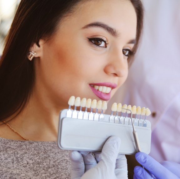 Cosmetic dentist in Durham holding shade guide next to smiling dental patient