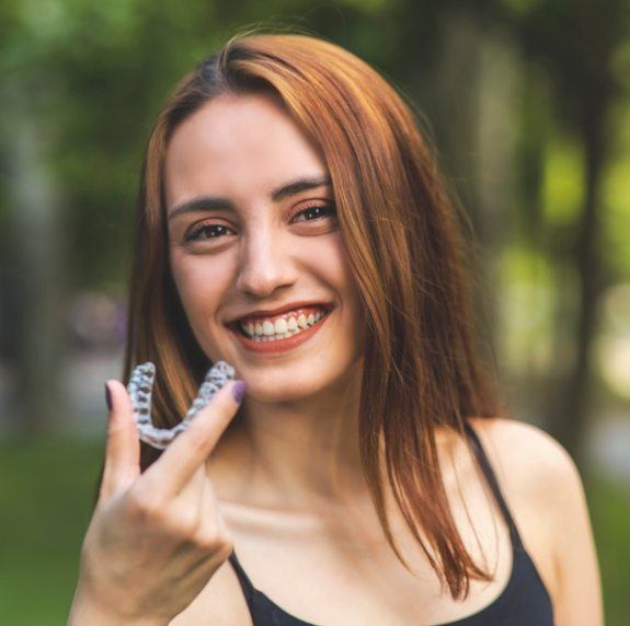 Smiling young woman holding Invisalign clear aligner in Durham