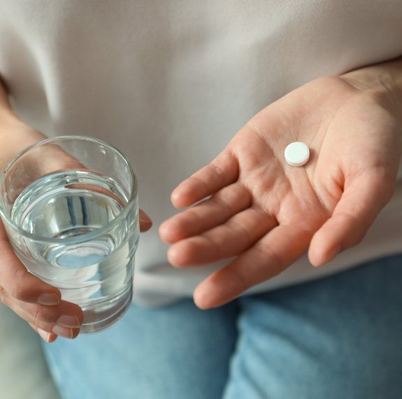 Person holding white pill and glass of water