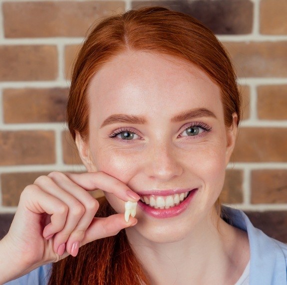 Smiling woman holding a tooth after tooth extraction in Durham